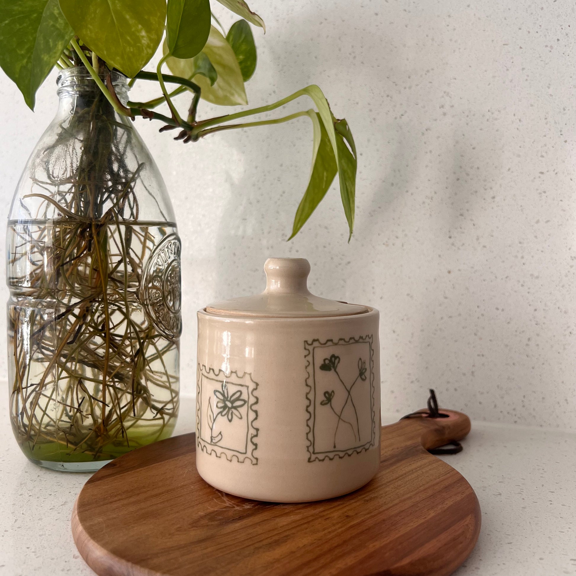 Decorative ceramic jar with a plant in a glass bottle on a wooden surface.