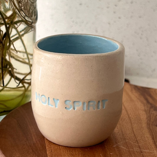 Ceramic cup with 'HOLY SPIRIT' text on a wooden surface