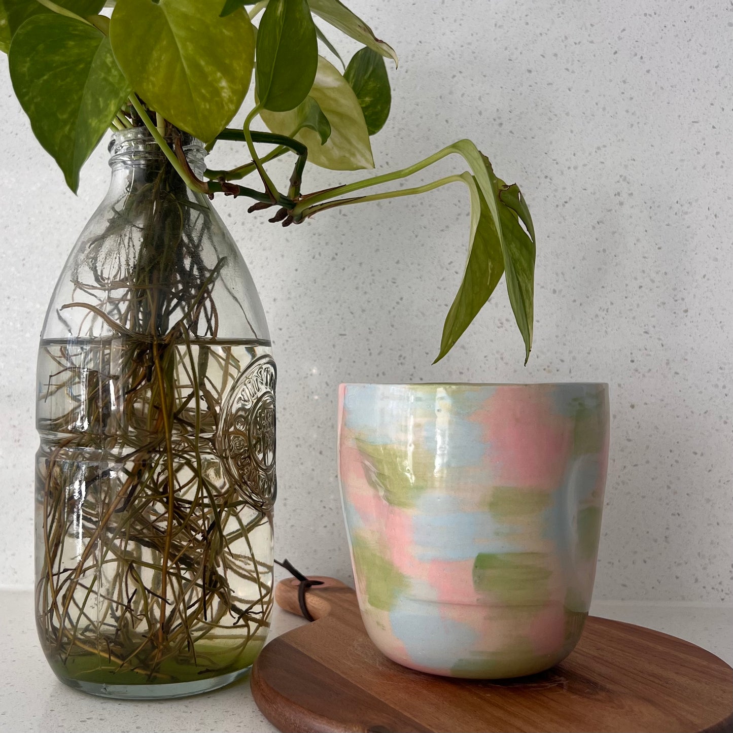 Clear glass vase with plant and colorful ceramic cup on a wooden surface