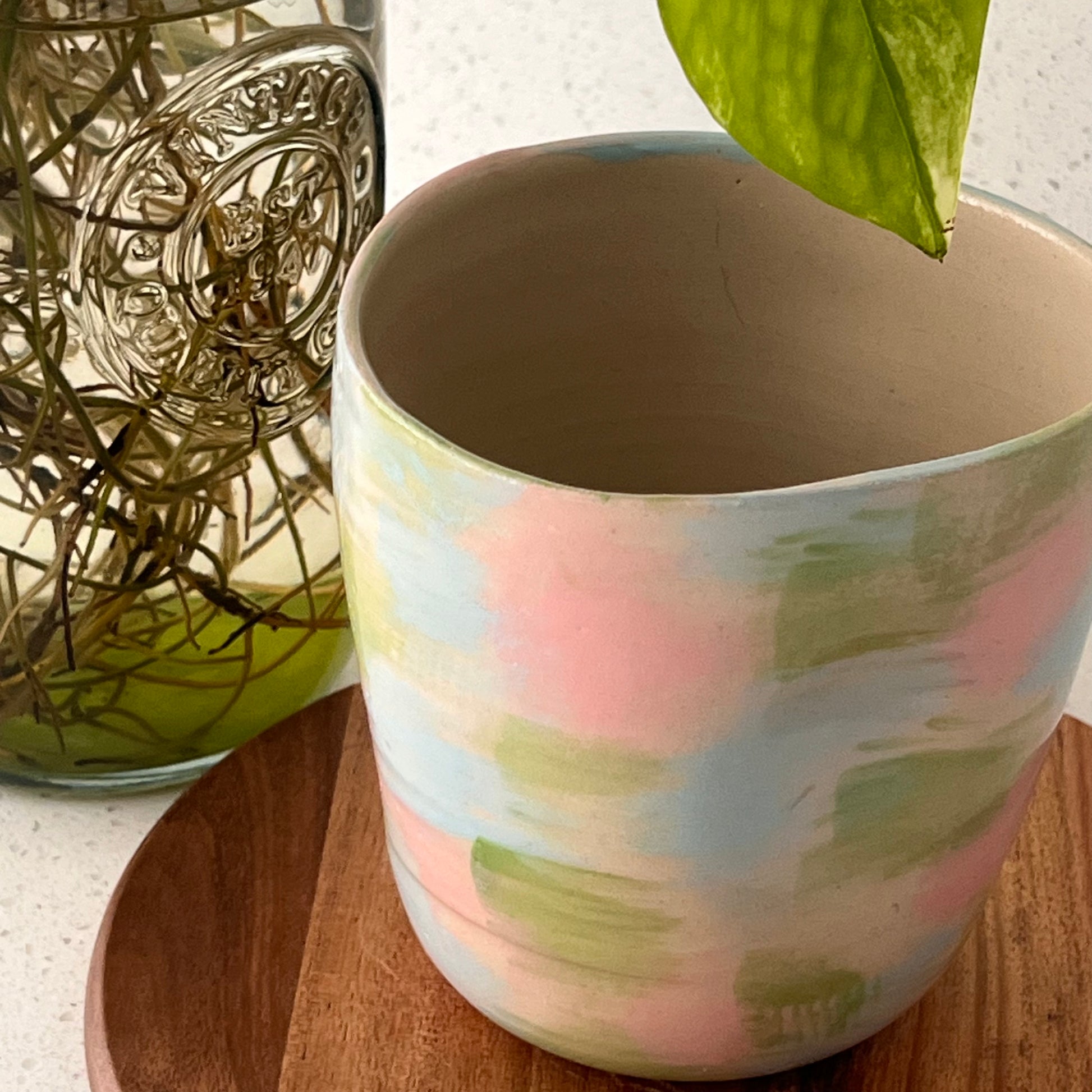 Ceramic mug with pastel design on a wooden surface next to a decorative glass jar.