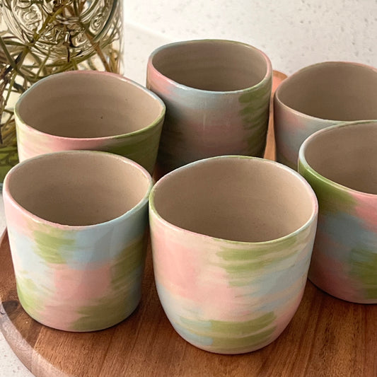 Set of ceramic cups with pastel color patterns on a wooden surface.